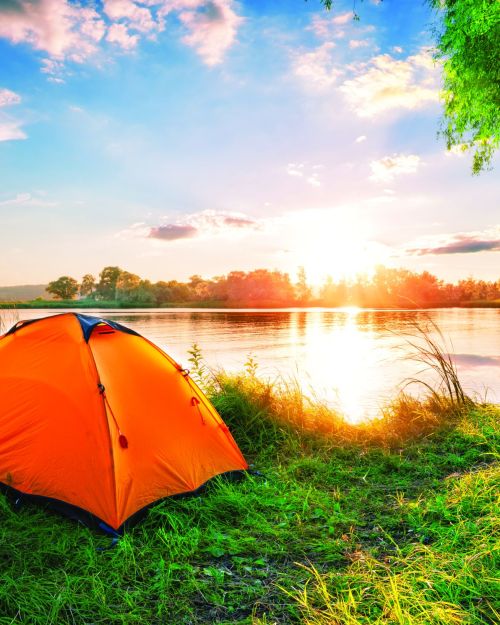 Orange tent on the lake at sunset. Bright sun. Summer landscape