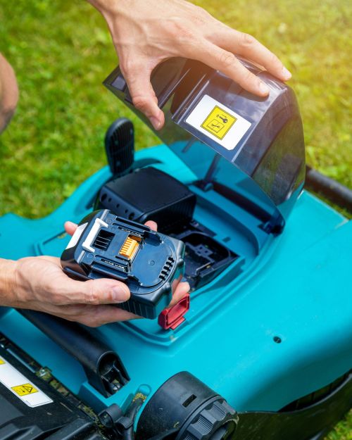 man putting battery into electric cordless lawn mower