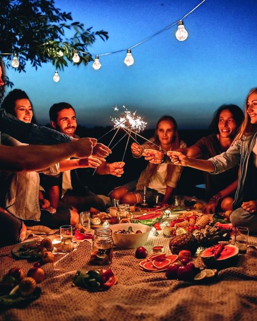 Happy friends having fun with fire sparkles. Young people millennials camping at picnic after sunset. Youth friendship concept on night mood